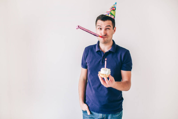 Νεαρός άνδρας απομονωμένος σε λευκό φόντο. Guy κατέχουν μικρό κέικ με κερί σε αυτό γιορτάζει τα γενέθλια. Μόνος στο πάρτι. Γιορτάζοντας μόνη. - Φωτογραφία, εικόνα