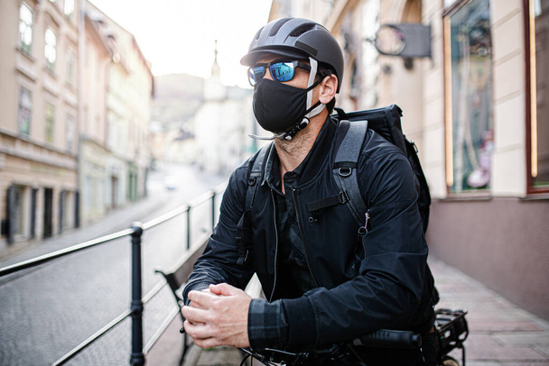 Delivery man courier with face mask and bicycle delivering parcels in town. - Valokuva, kuva