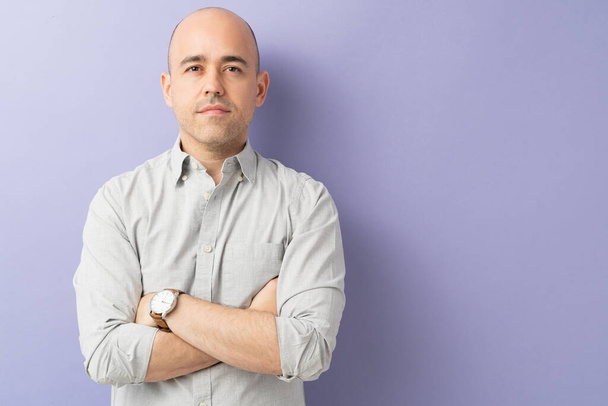 Attractive bald man in his 30s looking confident with arms crossed in a studio with purple background - Photo, Image