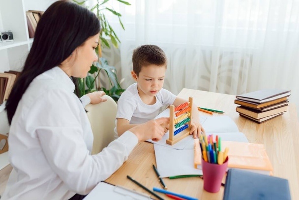 Female private tutor helping young student with homework at desk in bright child's room - Zdjęcie, obraz
