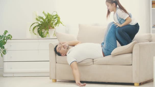 Father is tiered after playng with her little daughter on white sofa in 4k slowmotion video. - Materiał filmowy, wideo