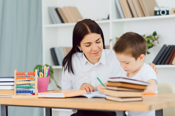 Young female tutor helping little elementary school boy with homework during individual lesson at home - Φωτογραφία, εικόνα