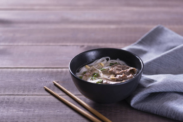 Asian cuisine, Vietnamese pho bo soup in a black plate on a wooden background - Foto, afbeelding