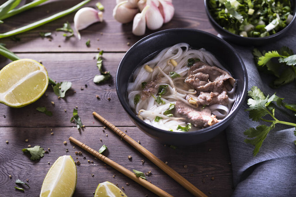 Asian cuisine, Vietnamese pho bo soup in a black plate on a wooden background - Foto, Imagen