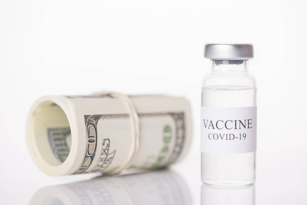 Дорогостоящая вакцина COVID-19 обрушилась на валютную концепцию. Крупным планом снимок пузырька с вакциной и стопка денег выделены на белом фоне
 - Фото, изображение