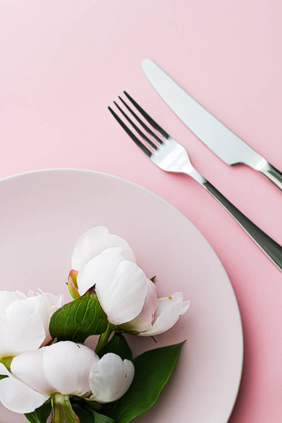 Eetbord en bestek met pioenroos bloemen als bruidsdecor op roze achtergrond, tafelgerei bovenaan voor de decoratie van evenementen en menubranding - Foto, afbeelding