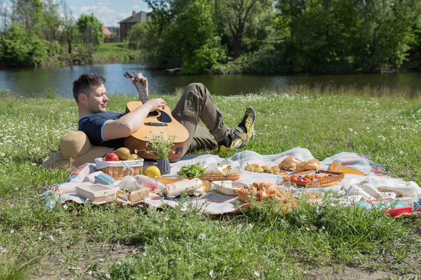 Young people doing picnic and playing guitar in park - Group of happy friends having fun during the weekend outdoor - Friendship, food and drink, funny activities and youth lifestyle concept - Photo, Image