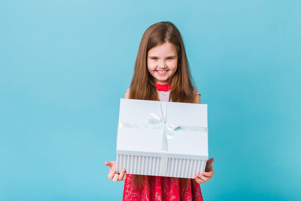 święta, prezenty, Boże Narodzenie, koncepcja dzieciństwa i urodziny - uśmiechnięta dziewczynka z pudełkiem na niebieskim tle - Zdjęcie, obraz