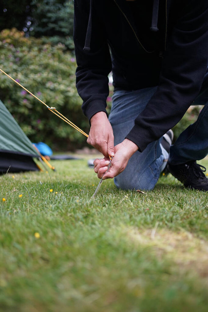 Крупный план мужских рук, прижимающих палатку к траве. Поставить палатку с колом
. - Фото, изображение
