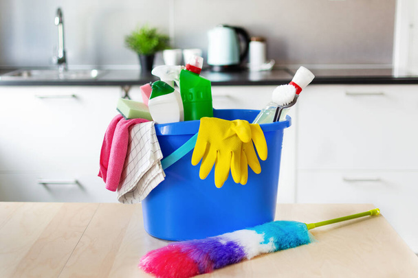 Bucket with bottles of detergent and cleaning equipment over kitchen interior. Household. Cleaning service idea. - Foto, Bild