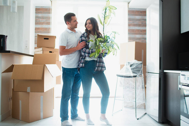 Ευτυχισμένο ζευγάρι με χαρτόκουτα, γλάστρα και ένα φυτό μέσα. Νέο σπίτι την ημέρα που κινείται. - Φωτογραφία, εικόνα