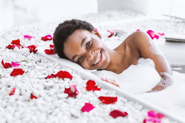 Wellnesstag und Schönheitspflege zu Hause. Frau badet mit Schaum und Blütenblättern - Foto, Bild