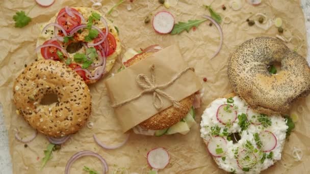 Bagels met ham, roomkaas, hummus, radijs verpakt in bruin bakpapier klaar om mee te nemen - Video
