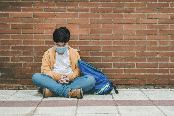 sad kid with medical mask and backpack sitting on the ground - Photo, Image