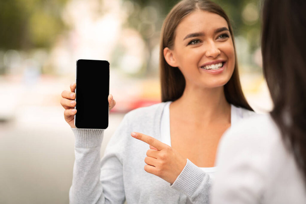 Girl Showing Smartphone Blank Screen To A Friend Walking Outside - Foto, Imagem