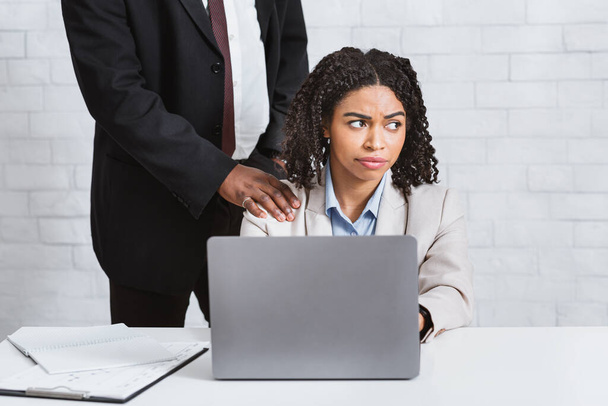 Sexuelles Fehlverhalten am Arbeitsplatz. Afroamerikanischer Chef berührt seine weiblichen Untergebenen im Amt an der Schulter - Foto, Bild