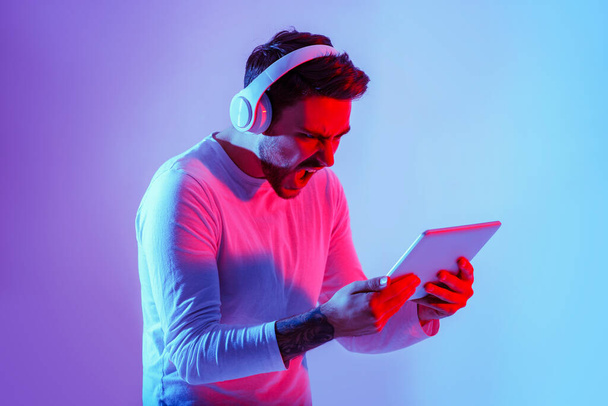 Συναισθηματικά online παιχνίδι. Ο τύπος με τα ακουστικά ουρλιάζει και παίζει σε tablet - Φωτογραφία, εικόνα