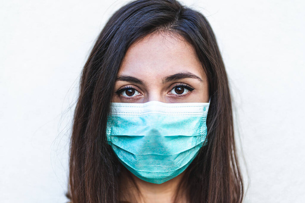 Close up portrait of a young woman wearing a protective surgical face mask and looking at camera, she is looking optimistic about epidemic end. Coronavirus oubreak and quarantine concept - Photo, Image
