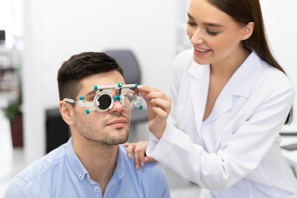 Οπτομετρητής που ελέγχει την όραση των ασθενών με πλαίσιο δοκιμής - Φωτογραφία, εικόνα