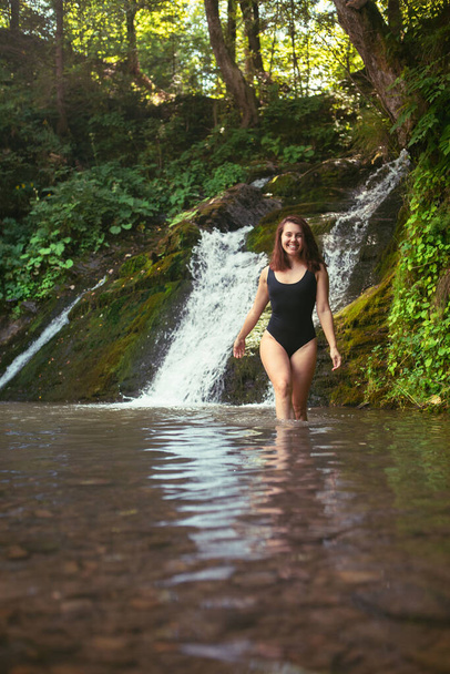 gorgeous woman in sexy black swimsuit in front of waterfall. copy space. summer time - Photo, Image