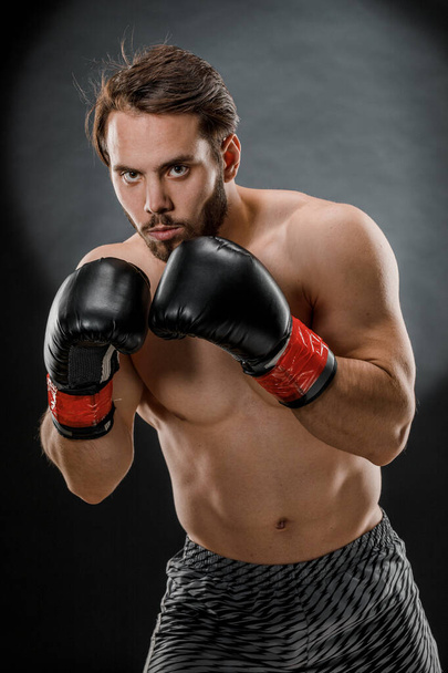 A man in Boxing gloves. A man Boxing on a black background. The concept of a healthy lifestyle. - Zdjęcie, obraz