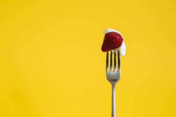 Makro záběr zralých jahod na vidličce s kyselou smetanou. Closeup červené bobule se žlutým pozadím - Fotografie, Obrázek