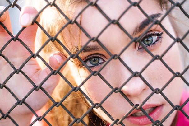 Candid ritratto di una ragazza con bellissimi occhi dietro una cattività recinzione metallica guarda dritto avanti desiderio di liberazione di uscire ed essere libero e la libertà
 - Foto, immagini