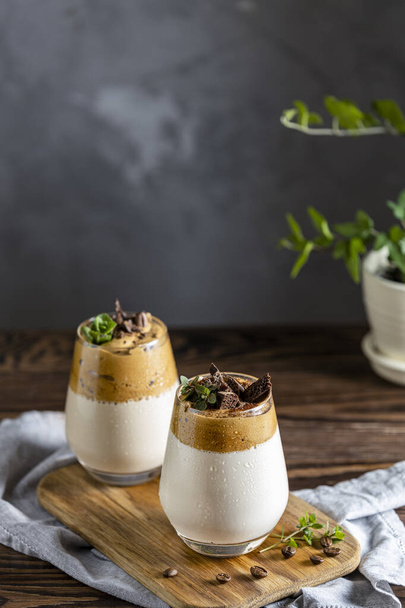Two glasses of Iced Dalgona Coffee, a trendy fluffy creamy whipped coffee, decorated by thyme and dark chocolate. Dark rustic style.	 - Foto, Imagen