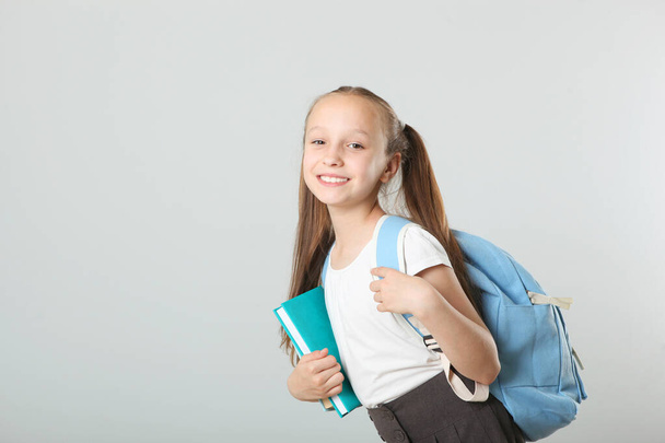 Portrait of a cheerful schoolgirl with a backpack and stationery on a light background. Place for text. Back to school. Preparations for school.National School Backpack Awareness Day - Фото, изображение
