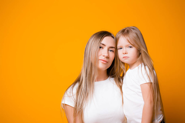 Mom and daughter are not happy that they are sitting on self-isolation. Portrait of a family on an orange background - Foto, Bild