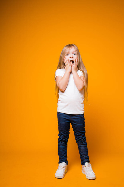 Portrait of a girl 4-7 years old stands on a yellow background and portrays surprise. children's emotions, happiness - Foto, Imagen