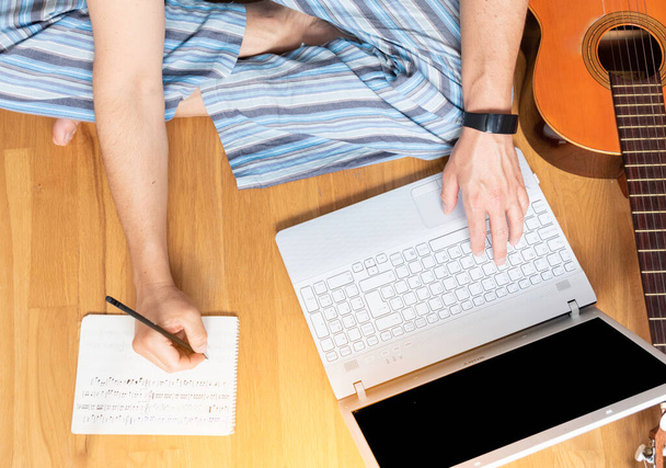 Muž sedící na podlaze a učící se hrát na kytaru. Zkontroluje laptop a dělá si poznámky.. - Fotografie, Obrázek