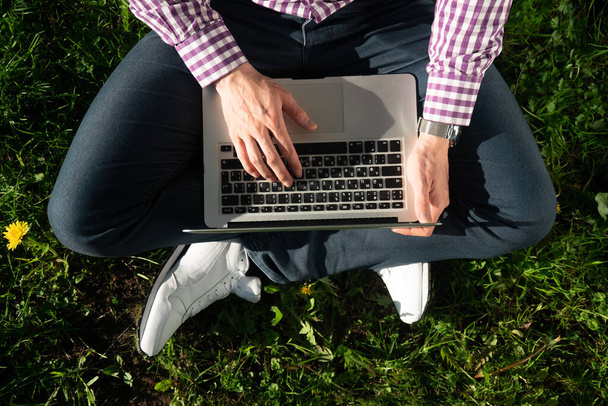 View from above , young man freelancer is sitting under a tree on a sunny day. working on a laptop. Online concept of online work in the park - 写真・画像