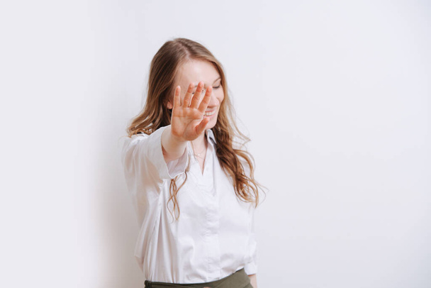 Shy young woman blocking camera with her hand. She doesn't want cameraman taking her picture. She has corporate look. Over white background. - Photo, image