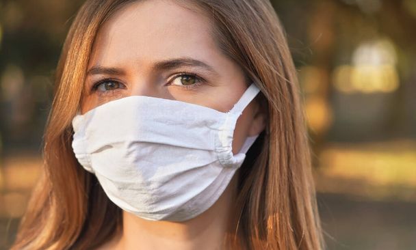 Young woman wearing white cotton virus mouth nose mask, nice bokeh in background, closeup face portrait - 写真・画像