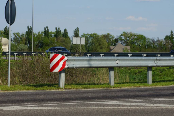 barrera de hierro largo gris con una astilladora rayada de un camino de asfalto contra un cielo azul
 - Foto, Imagen