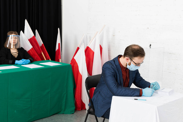 Ο άνθρωπος κάθεται στην καρέκλα μπροστά από την εκλογική κάρτα. Επιλέγει έναν υποψήφιο. Συμπληρώνει το ψηφοδέλτιο. - Φωτογραφία, εικόνα