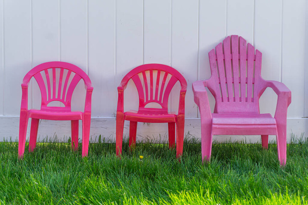 Petites chaises en plastique colorées contre une clôture en bois blanc
 - Photo, image