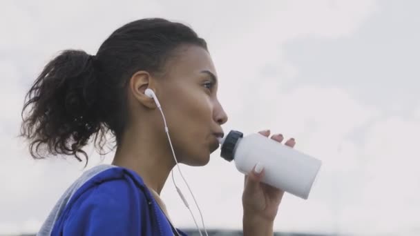 Афро-американская бегунья, пьющая воду или изотоническая после бега. Портрет Фитнес-женщина пьет воду из бутылки
. - Кадры, видео