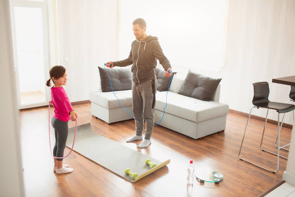 father and daughter are training at home. Workout in the apartment. Sports at home. They use a rubber rope for training - Foto, imagen