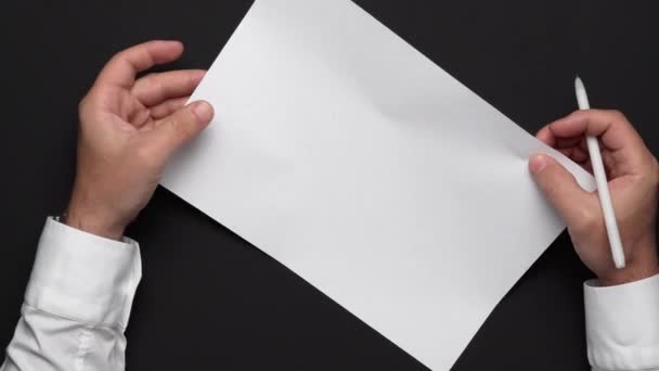 πάνω όψη ενός λευκού φύλλου χαρτιού και των χεριών ενός επιχειρηματία σε ένα μαύρο τραπέζι, λευκό πουκάμισο και ρολόι καρπού - Πλάνα, βίντεο