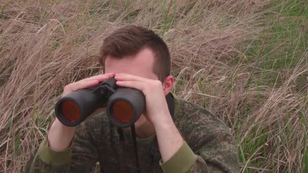 the guy watches through binoculars sitting in the bushes - Footage, Video