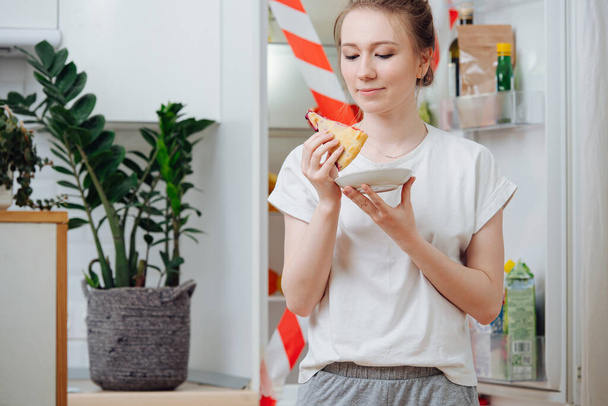Mujer comiendo rebanada de pastel delante del frigorífico sellado con cinta adhesiva
 - Foto, Imagen
