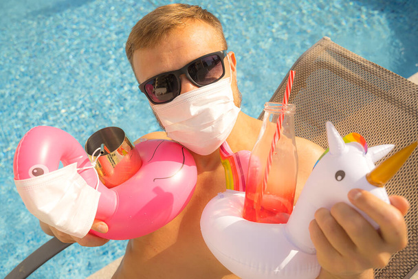 Modèle masculin caucasien sur une chaise de plage à côté d'une piscine portant un masque facial, tenant des jouets gonflables de piscine
 - Photo, image