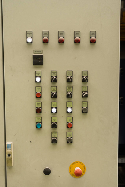lähikuva sähköisestä ohjauspaneelista, jossa on kytkimet, moniväriset osoittimet ja hätäpysäytys
 - Valokuva, kuva