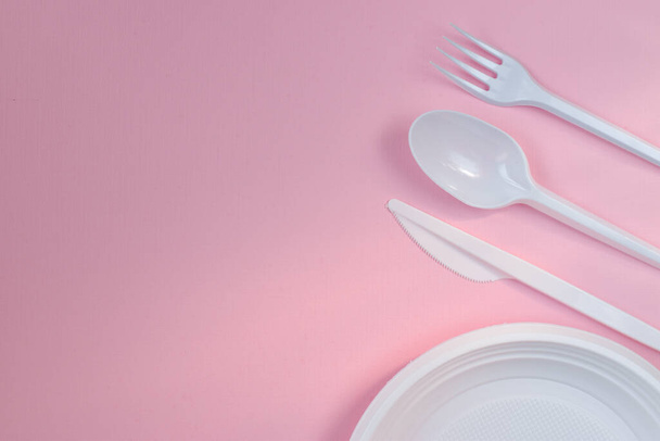 Plastic white utensils on a pink background from the right. - Fotografie, Obrázek