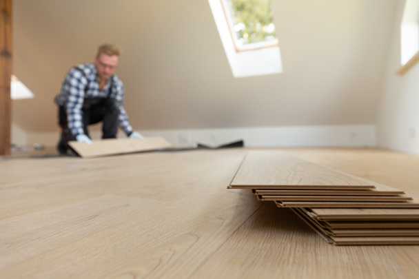 Építési munkás telepítése laminált padló egy új felújított padláson. Háztartási javítási koncepció. - Fotó, kép