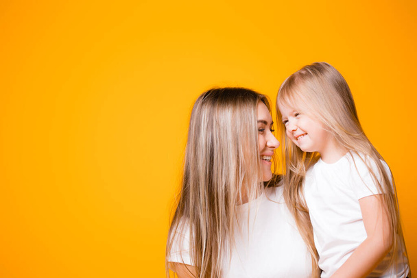 Mom and daughter hug each other and smile on an orange background. Happy family relationships - Valokuva, kuva
