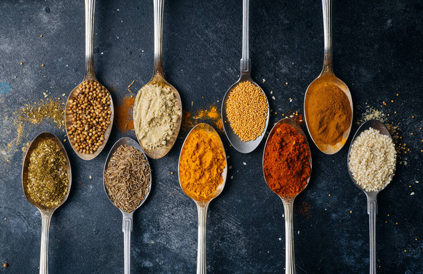 Spices in spoons background. Varieties of spices (turmeric, pepper, chili, coriander, cinnamon) and peppers for cooking. Culinary food concept. - Photo, Image