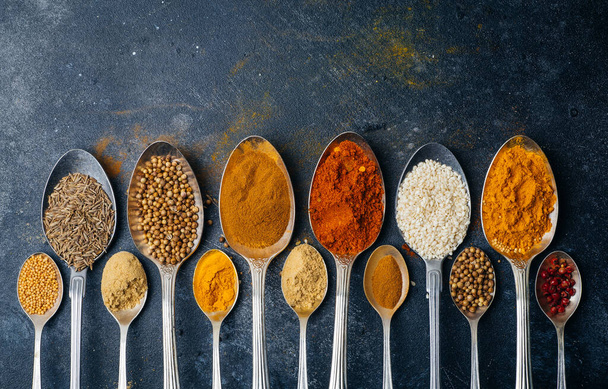 Spices in spoons background. Varieties of spices (turmeric, pepper, chili, coriander, cinnamon) and peppers for cooking. Culinary food concept. - Photo, Image